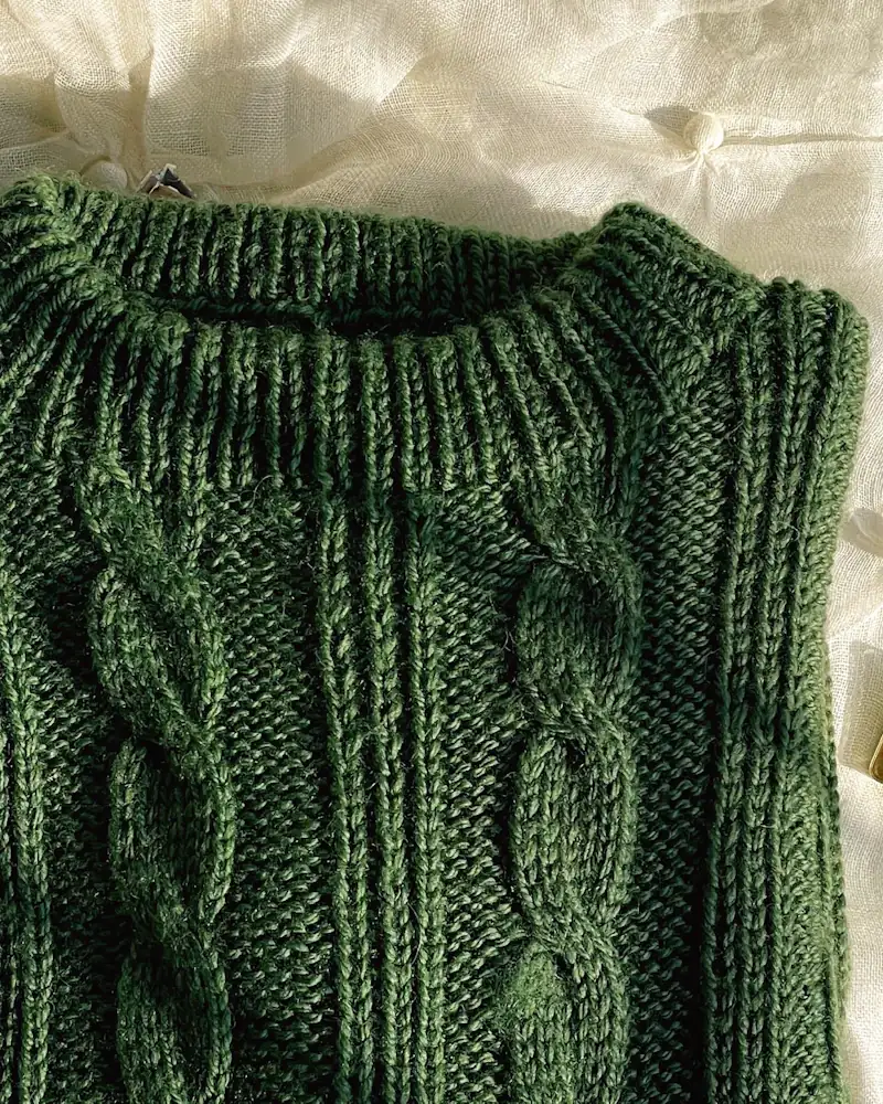 Moss green cable knit jumper laid flat, close-up